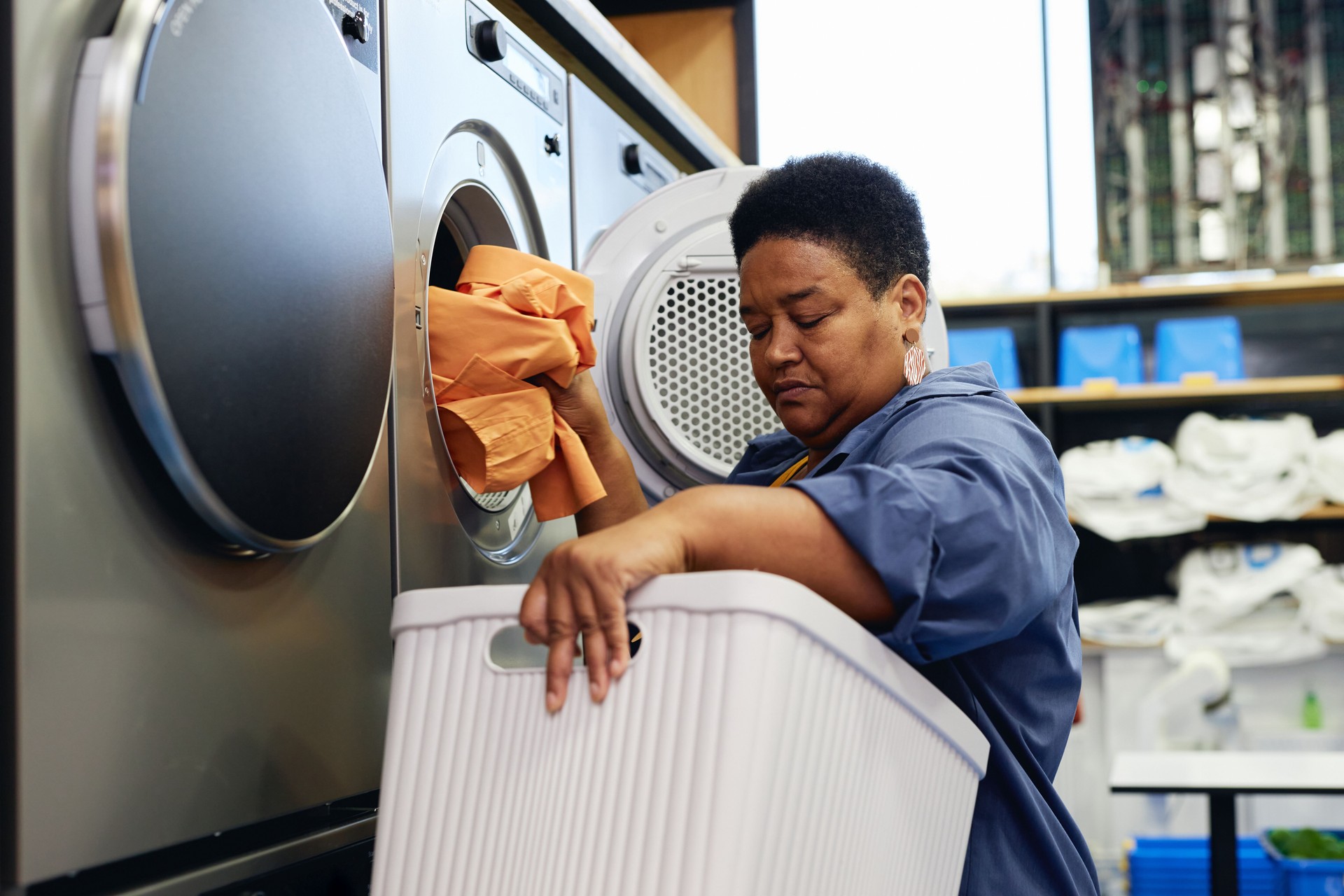 Senior Black Woman Placing Clothes from Basket into Washer at Self Service Laundromat