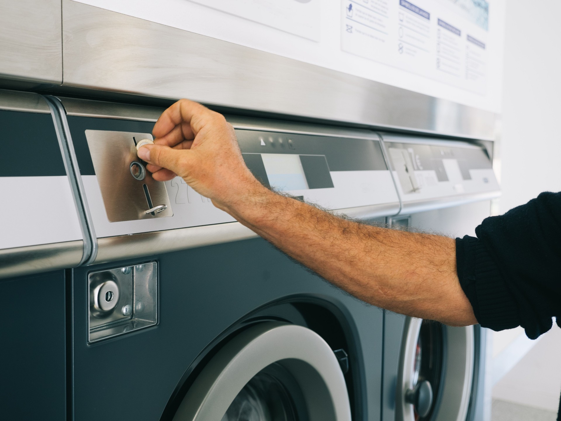 Hands of man selecting coins for washing machine at laundrette.